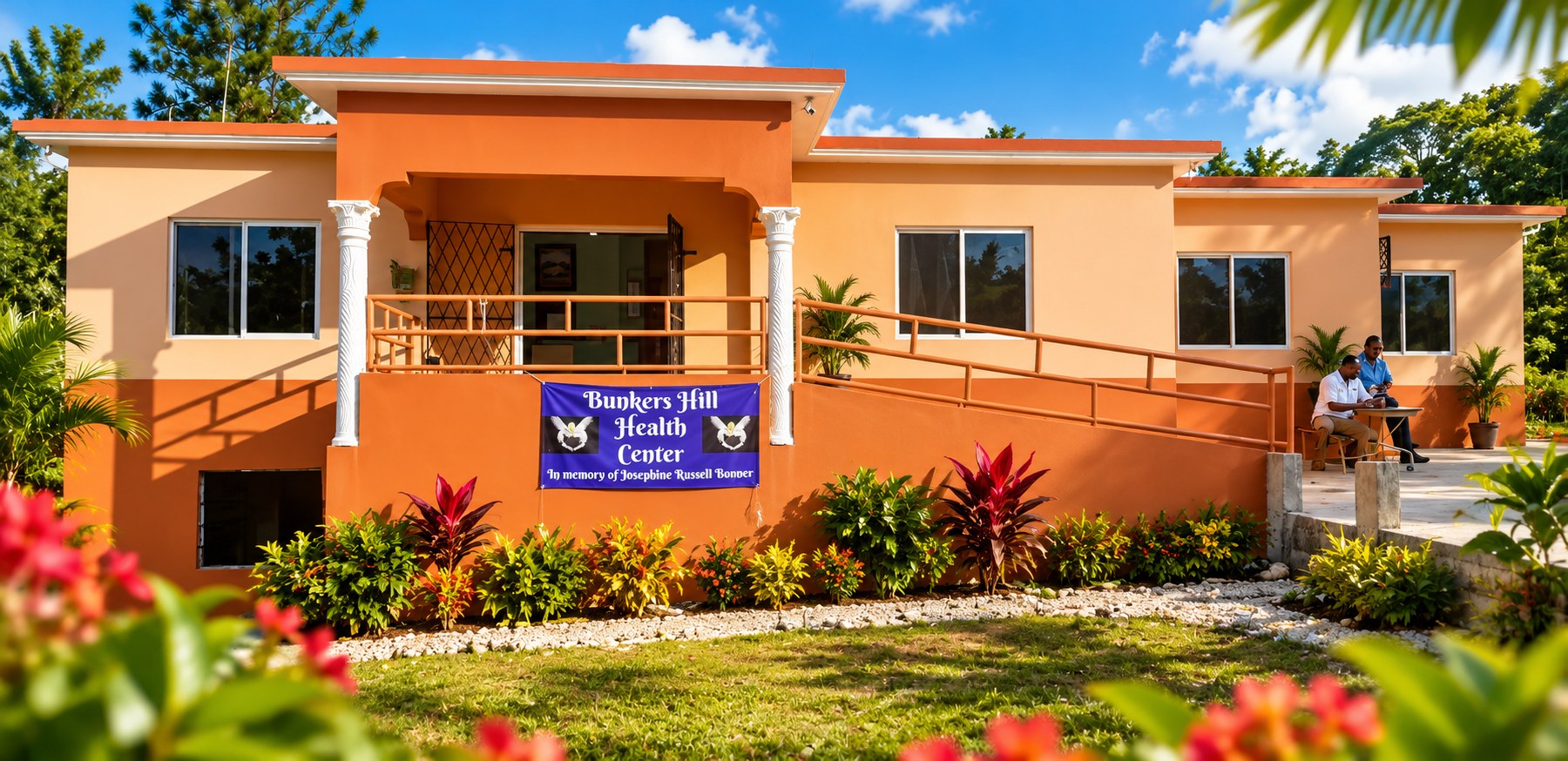 The Bunkers Hill Community Health Center in Jamaica, its peach walls and white porch columns, with a blue banner on the porch railing reading Bunkers Hill Health Center, in memory of Josephine Russell Bonner